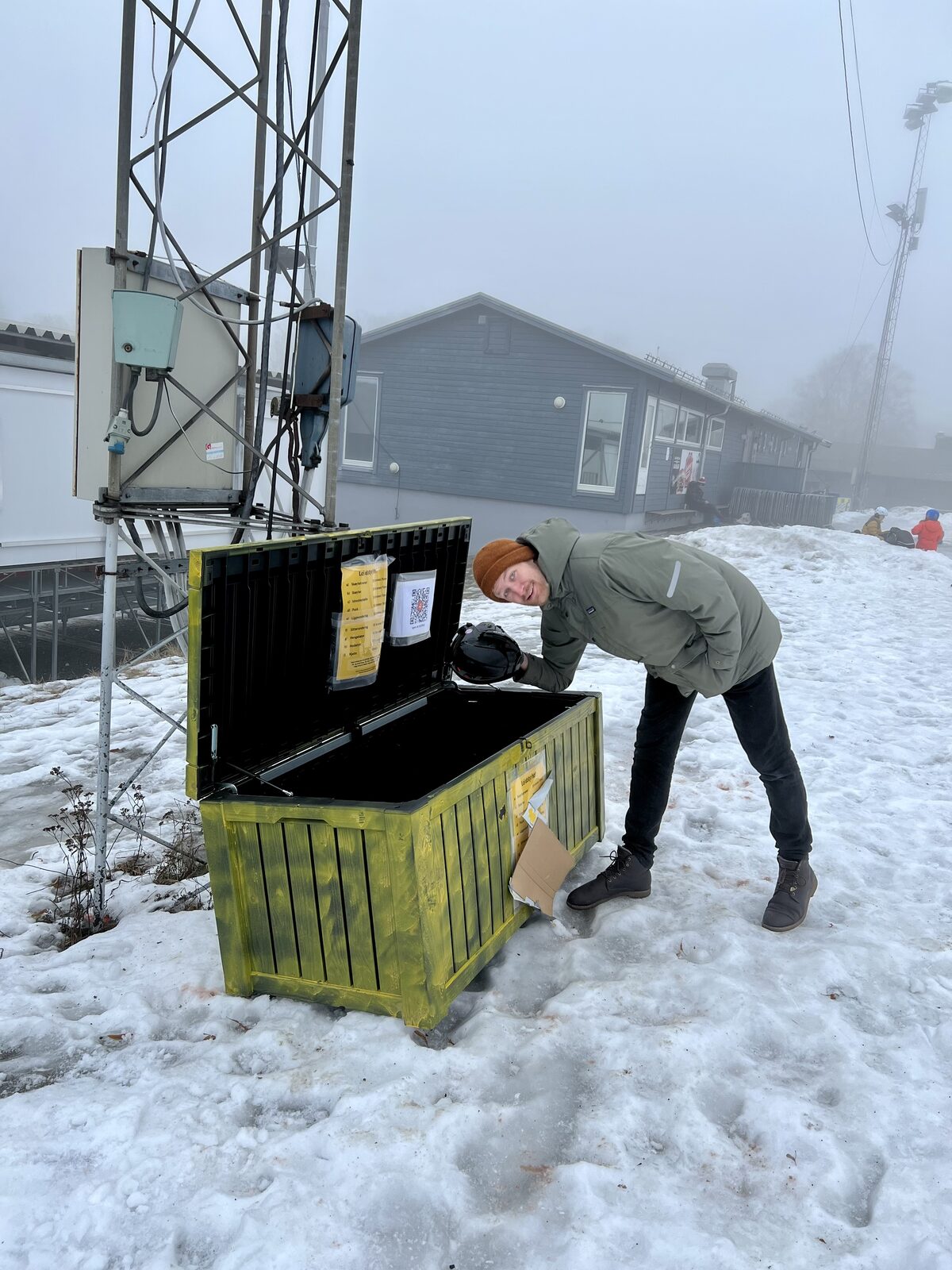 Person åpner et gult Haralt-utleieskap i skibakken og henter ut en skihjelm